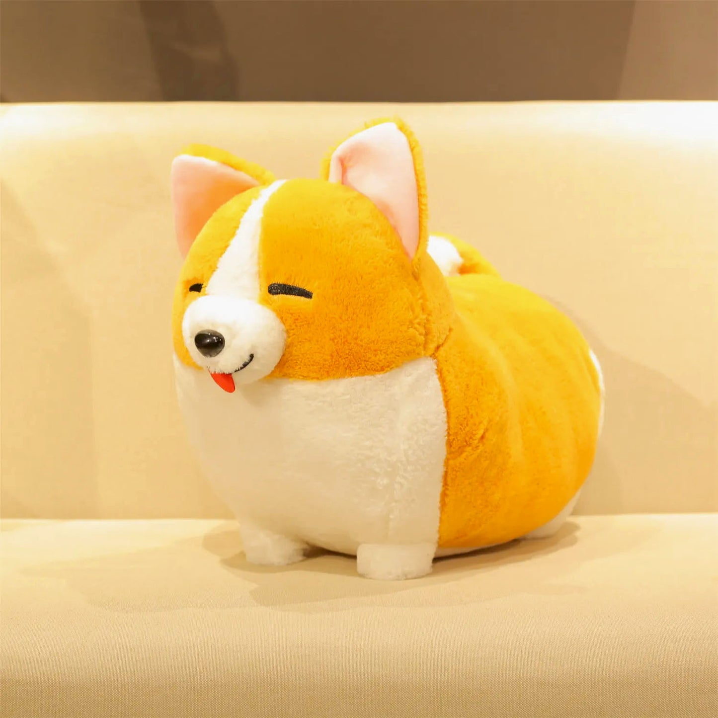 A plush Corgi dog toy with a yellow-orange and white color scheme, sitting on a beige sofa.