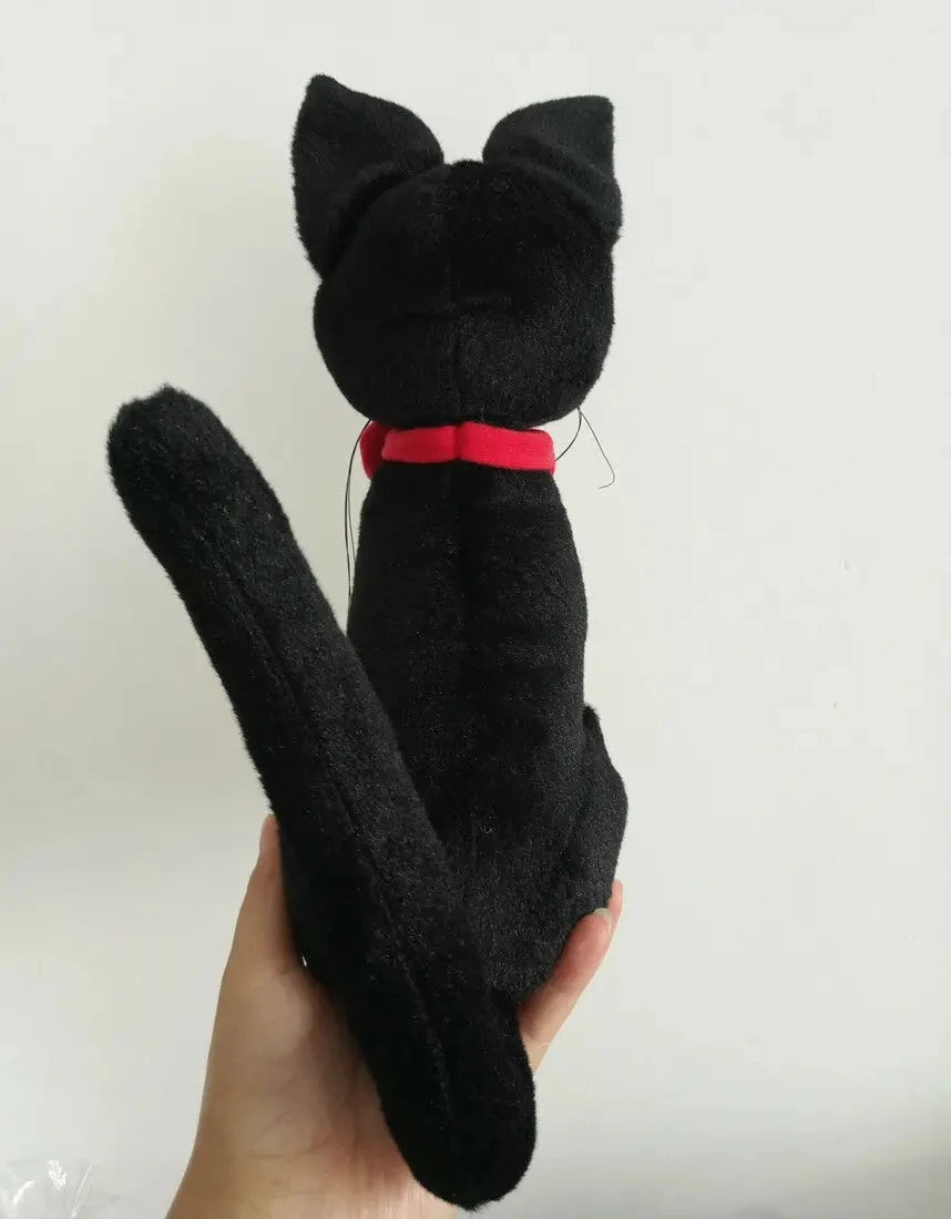 Black cat-shaped plush toy with a red bow held by a hand on a white background