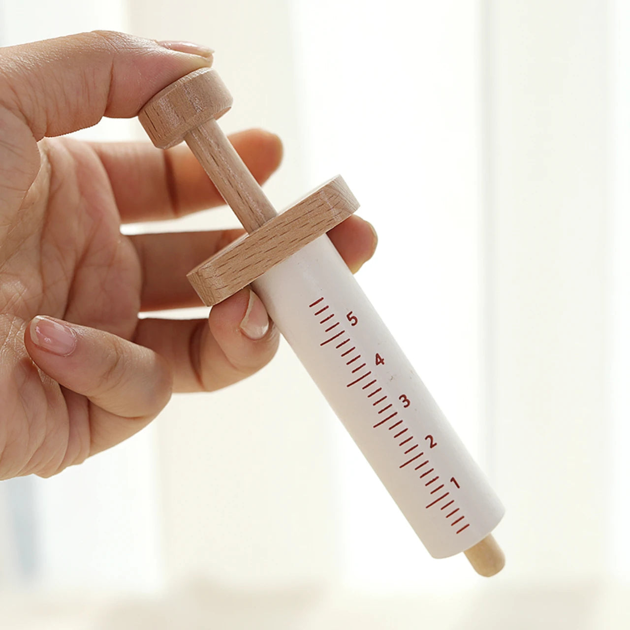 Hand holding a wooden syringe with measurement markings against a blurred background