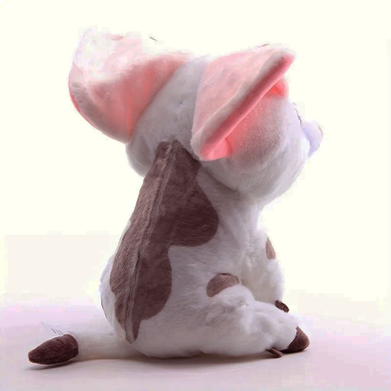 A white and brown spotted plush toy dog sitting on a light pink surface against a pale background.