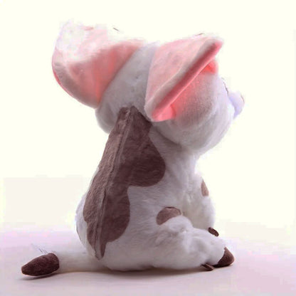 A white and brown spotted plush toy dog sitting on a light pink surface against a pale background.