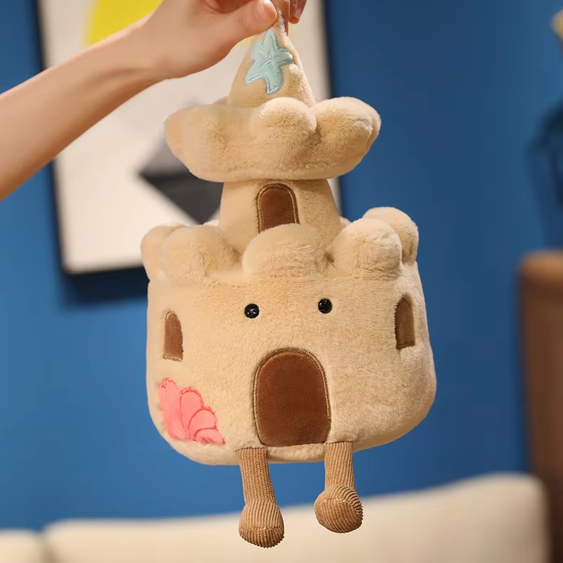 Plush toy shaped like a cloud with a house on top, held by a hand against a blue wall.
