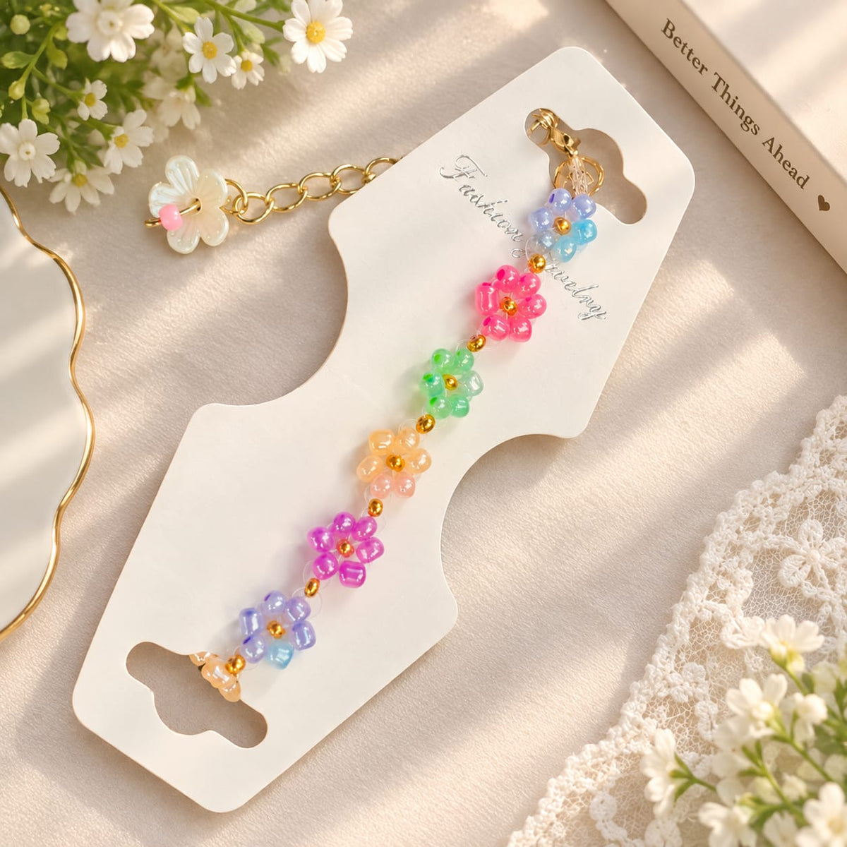 A colorful beaded flower keychain with gold-tone chain and clasp, displayed on a white card with decorative flowers and lace around it.