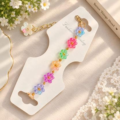A colorful beaded flower keychain with gold-tone chain and clasp, displayed on a white card with decorative flowers and lace around it.