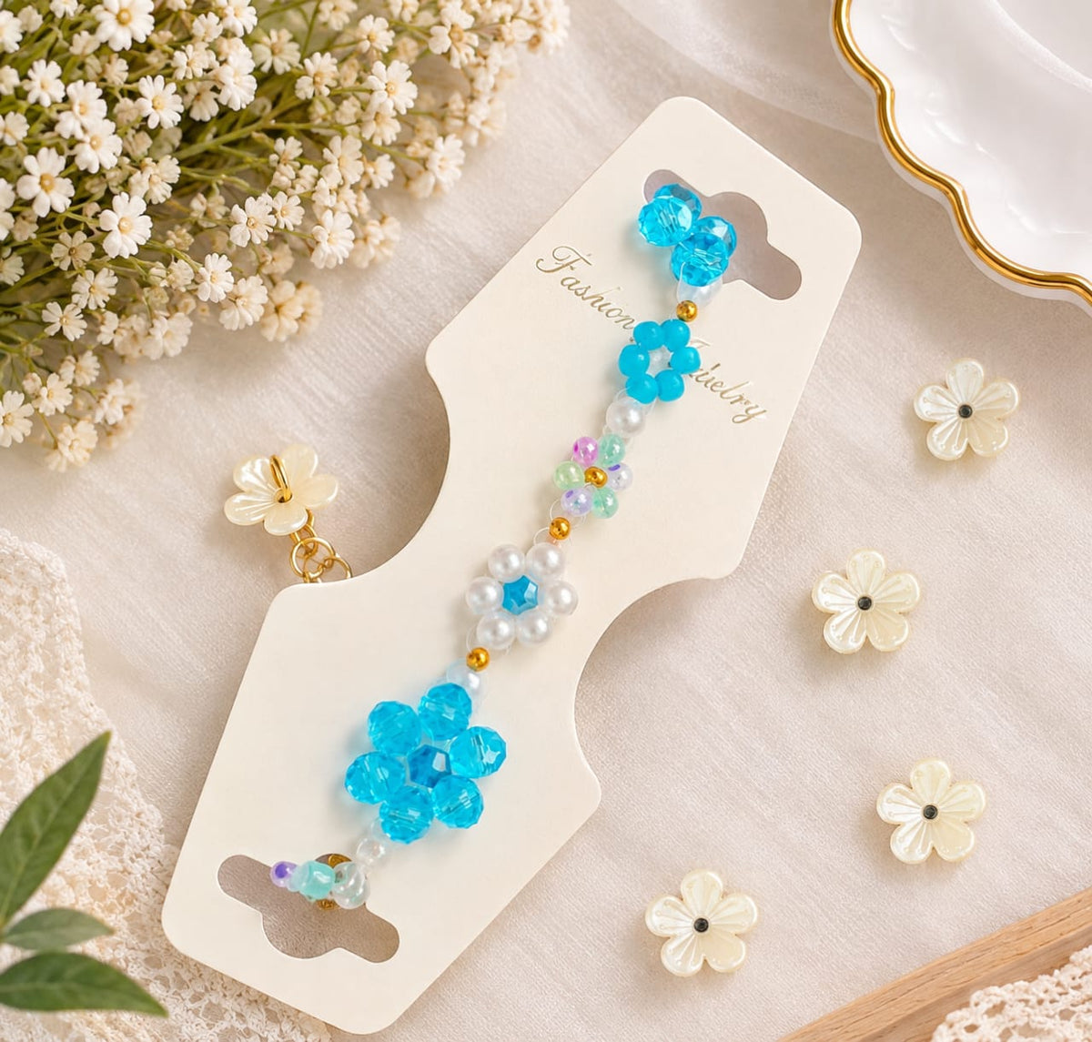 A beaded women's bracelet on a cream-colored card, surrounded by small white flowers and lace on a light fabric background.