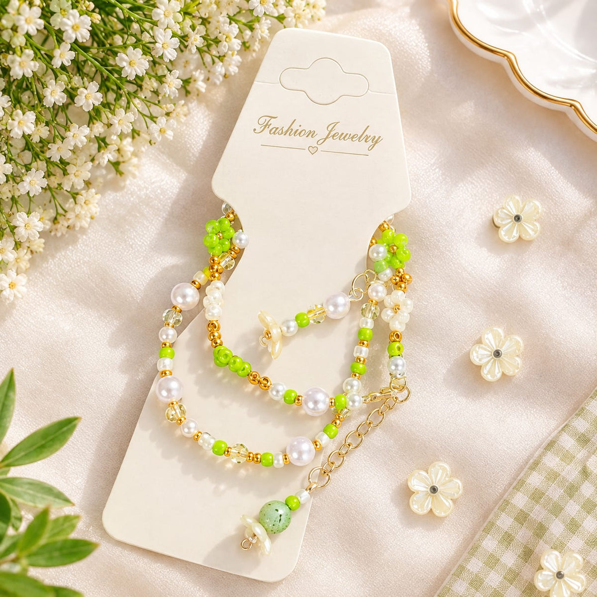 A pair of beaded and pearl chain earrings displayed on a white card labeled 'Fashion Jewelry,' styled with small white flowers and green leaves on a soft cream fabric background.