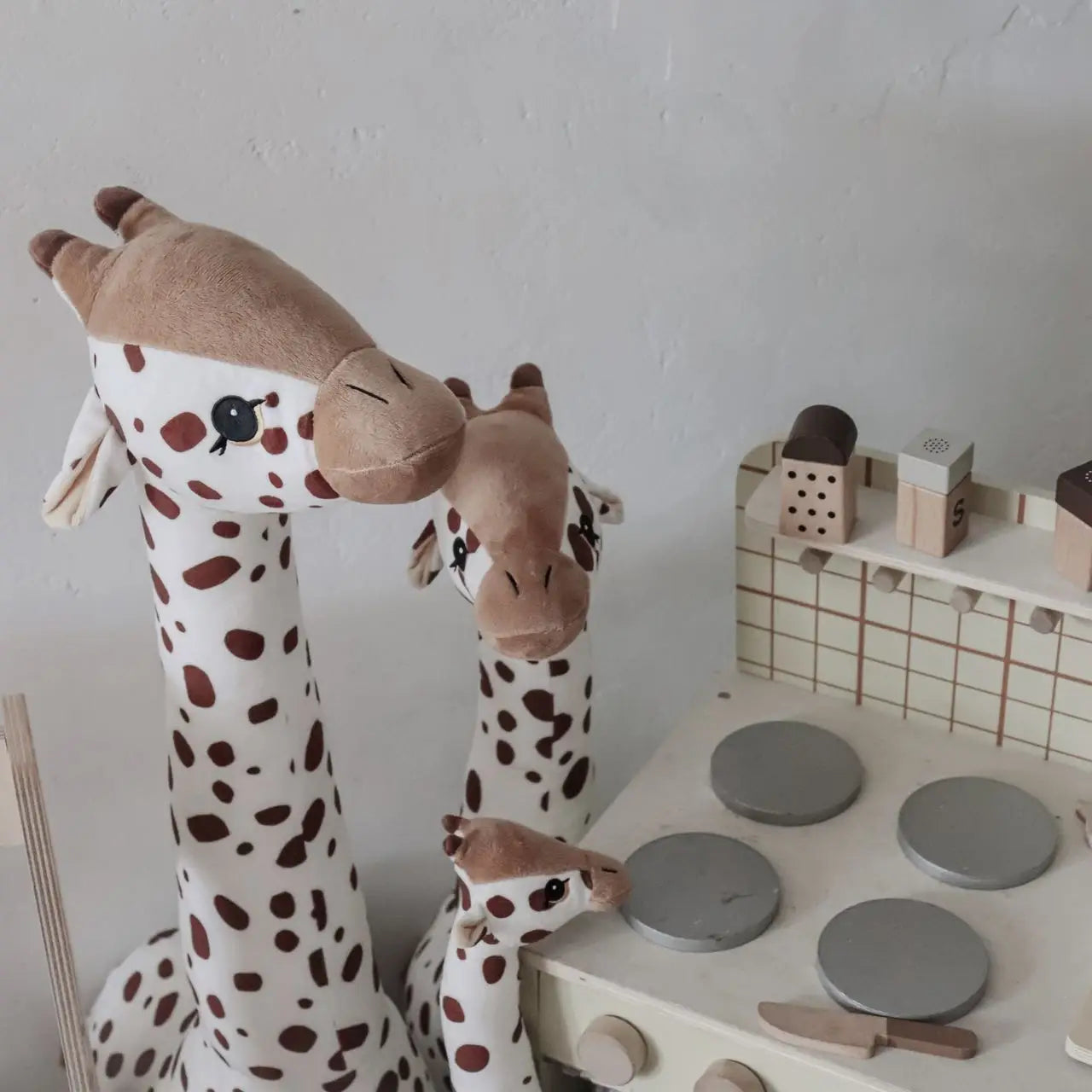 Plush giraffe toy next to a child's play kitchen set on a white wall background