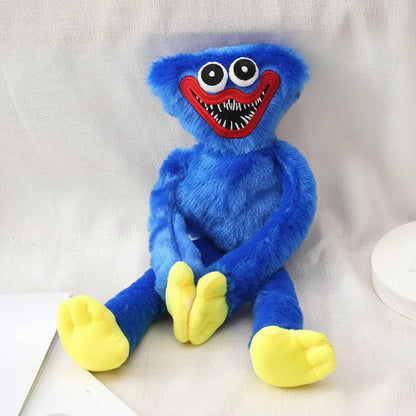 A blue furry plush toy resembling a cartoon monster with large white eyes, a wide red mouth, and yellow feet, posed against a light fabric backdrop.