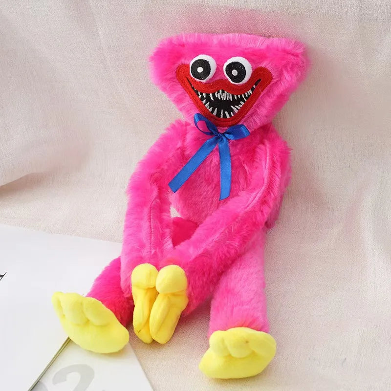 huggy wuggy character plush toy with large white eyes, a red mouth showing white teeth, and a blue ribbon bow, sitting on a light fabric background.