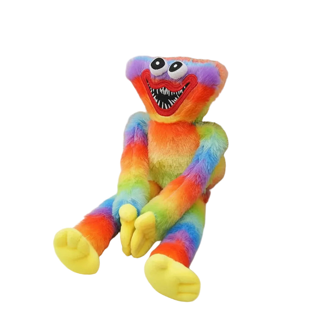 A plush toy resembling a rainbow monster with bright multicolor fur, large round eyes, a wide toothy grin, and yellow feet, posed on a light fabric surface beside a woven basket.