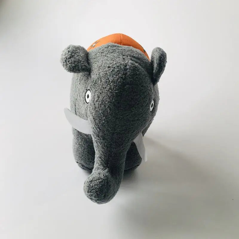 A plush elephant toy in dark gray with white tusks and a small orange hat on its head, photographed against a plain light gray background.